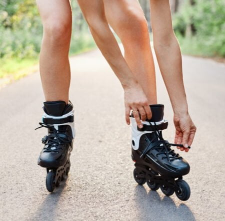 Woman lace up roller skates while rollerblading outdoor summer park asphalt road