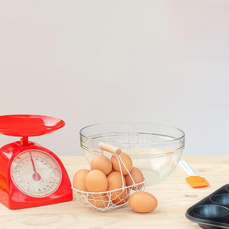 Analog kitchen scale with raw ingredients for a cake on a wooden table