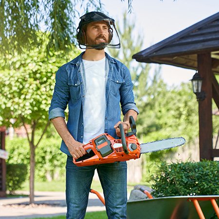 Strong male gardener in protective shield holding cordless chain saw