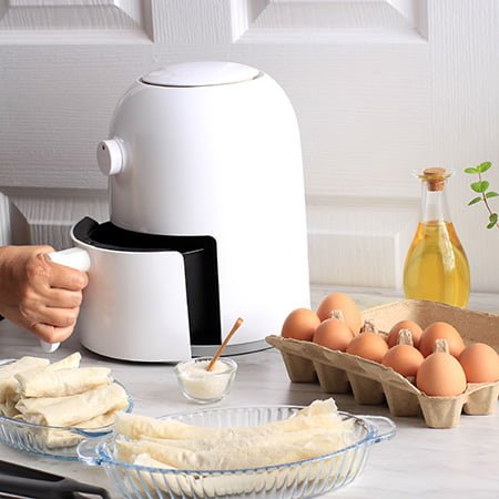 White airfryer on kitchen countertop with pancakes and ingredients